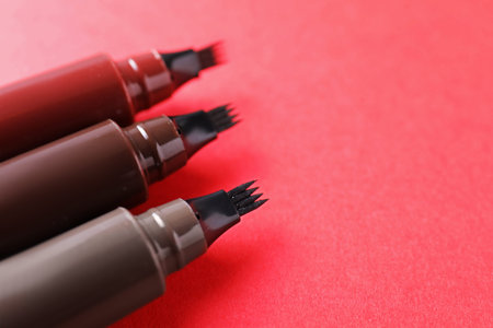 Liquid eyebrow pencils on red background, closeup. Space for text
