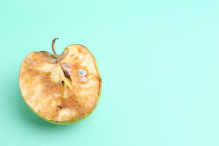 Half of spoiled apple on turquoise background, top view. Space for text