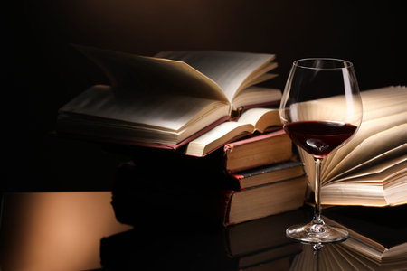 Red wine in glass and stack of books on mirror table against dark background, closeupの写真素材
