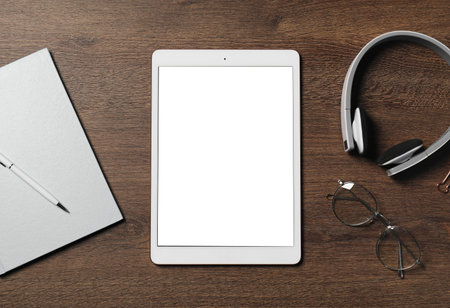 Tablet, headphones, glasses and stationery on wooden table, flat lay