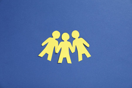 Human paper figures holding hands on blue background, flat lay