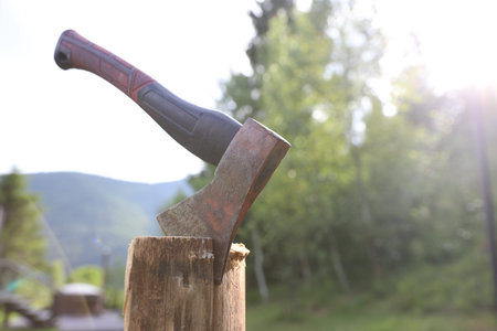 Metal ax on wooden log outdoors, closeup. Space for text