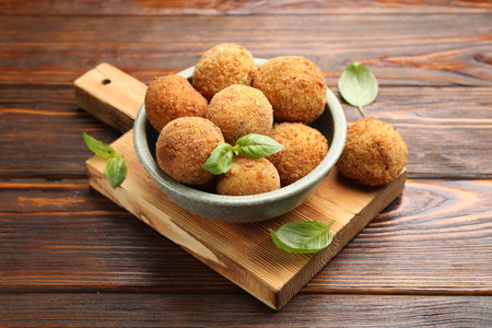 Delicious fried croquette balls with basil in bowl on wooden table, closeup