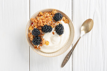 Tasty yogurt with granola and blackberries in bowl on white wooden table, top viewの写真素材