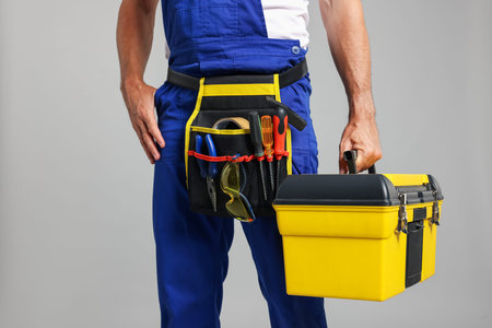 Professional repairman with tool box on gray background, closeup