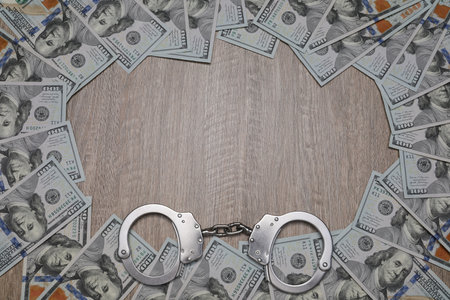 Corruption. Handcuffs and dollar bills on wooden table, flat lay. Space for textの写真素材