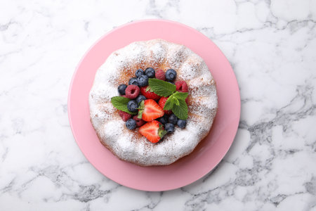 Tasty Bundt cake with powdered sugar and berries on white marble table, top view