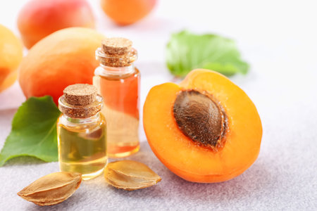 Aromatic essential oil in bottles, seeds and ripe apricots on light textured table, closeup