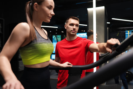Young woman exercising on treadmill with professional personal trainer in gymの写真素材