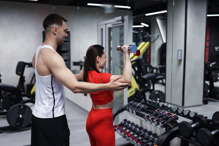 Young woman exercising with dumbbells with professional personal trainer in gym
