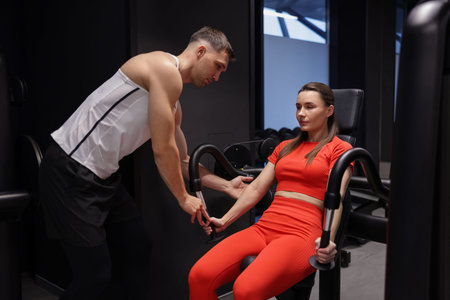 Young woman exercising with pull down machine professional personal trainer in gym