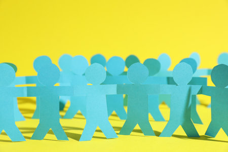 Human paper figures holding hands on yellow background, closeupの写真素材