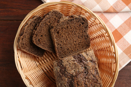 Pieces of fresh rye bread in wicker basket on wooden table, top view