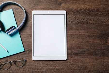 Tablet, headphones, glasses and stationery on wooden table, flat lay. Space for text
