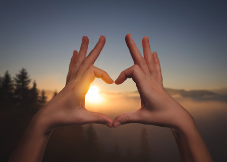 Hope. Woman making heart with hands against sun in mountains, closeupの写真素材