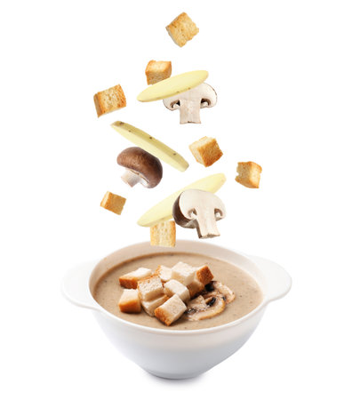 Croutons, mushrooms and potato slices falling into bowl of soup against white backgroundの写真素材