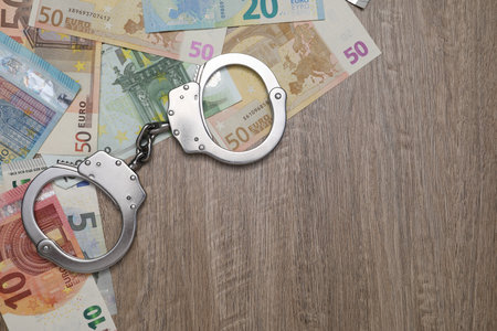 Corruption. Handcuffs and euro banknotes on wooden table, flat lay. Space for textの写真素材