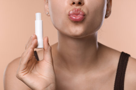 Young woman with lip balm on beige background, closeupの写真素材