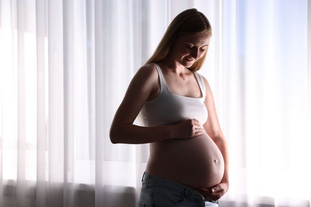 Beautiful pregnant woman near window at home