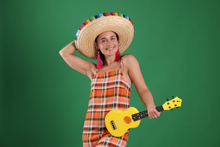 Smiling woman in sombrero hat with ukulele on green background