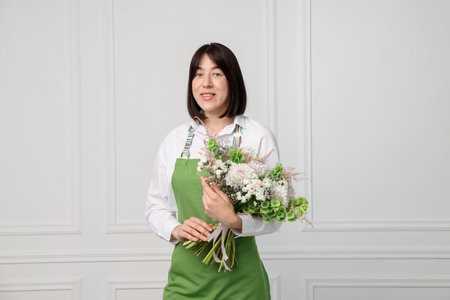 Florist with beautiful bouquet of flowers near white wall indoorsの写真素材
