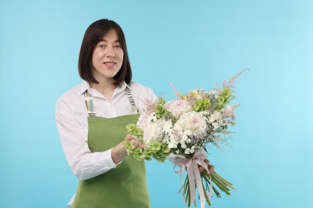Florist with beautiful bouquet of flowers on light blue backgroundの写真素材