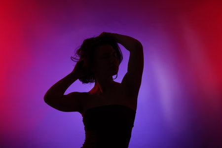 Silhouette of woman posing in neon lights on color backgroundの写真素材