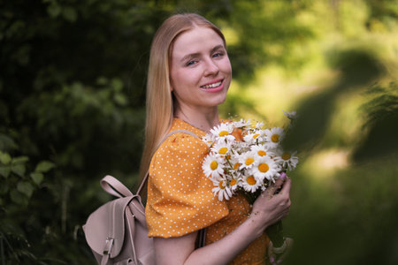 Beautiful woman with bouquet of wildflowers and backpack in forestの写真素材