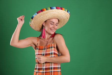 Smiling woman in sombrero hat dancing on green background. Space for textの写真素材