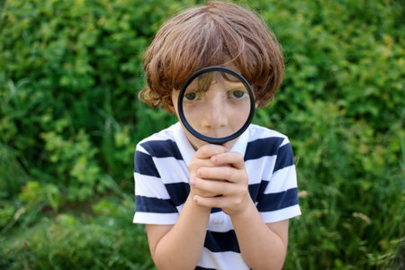 Cute little boy looking through magnifying glass in natureの写真素材
