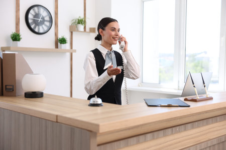 Smiling receptionist talking with client by phone at reception desk in hotelの写真素材