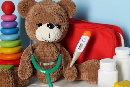 Pediatrician concept. Toys, first aid kit, pills, thermometer and stethoscope on white wooden table against light blue background, closeupの写真素材