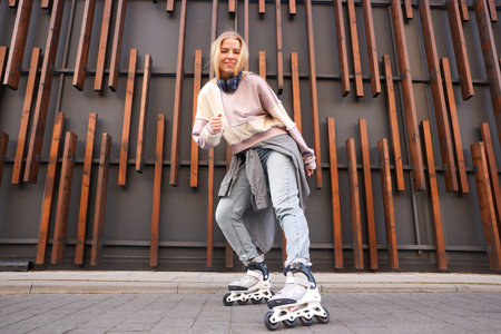 Beautiful young woman with roller skates near building outdoors, low angle view