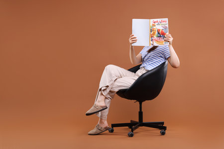 Woman with lifestyle magazine on armchair against brown background, space for textの写真素材