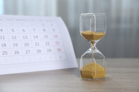 Deadline. Hourglass with flowing sand and calendar on wooden table indoorsの写真素材