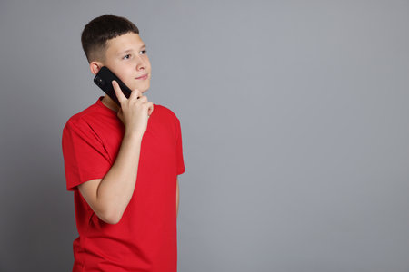 Teenage boy talking on smartphone against grey background, space for textの写真素材