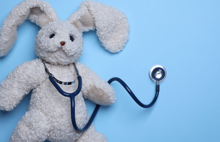 Pediatrics concept. Toy bunny with stethoscope on light blue background, top view. Space for textの写真素材