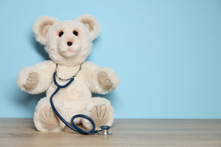 Pediatrician concept. Toy bear and stethoscope on wooden table against light blue background, space for textの写真素材