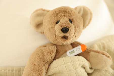 Pediatrics concept. Toy bear with thermometer in bedの写真素材