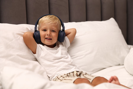 Cute little boy in headphones on bedの写真素材