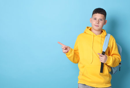 Teenage boy with backpack pointing at something on light blue background, space for textの写真素材