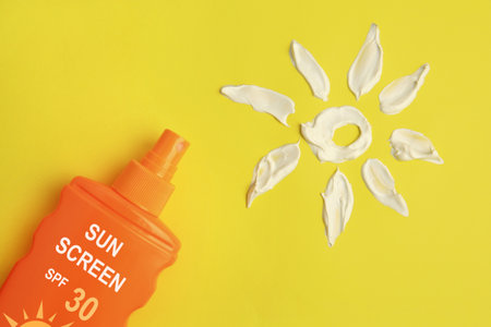 Sunscreen in bottle and sun made of sun protection cream on yellow background, top viewの写真素材
