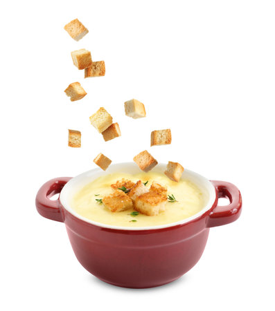 Croutons falling into bowl of soup against white backgroundの写真素材