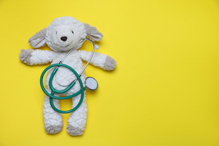 Pediatrics concept. Toy sheep with stethoscope on yellow background, top view. Space for textの写真素材
