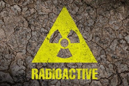Yellow radioactive sign on cracked dry earth, top view. Radiological pollution
