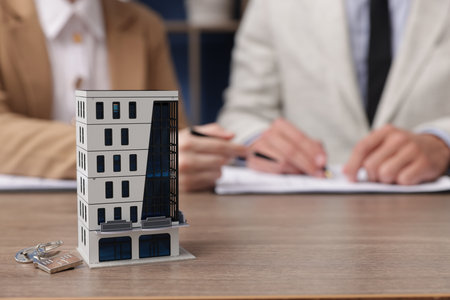 Real estate agent working with client at desk in office, focus on house modelの写真素材