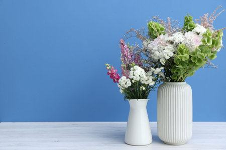 Beautiful flowers in vases on white wooden table against light blue background, space for textの写真素材