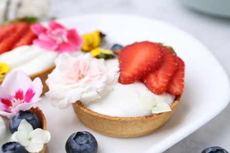 Sweet tartlets with berries and flowers on light table, closeup. Delicious dessertの写真素材