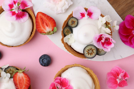 Delicious dessert. Tartlets with cream, berries and flowers on pink background, flat layの写真素材