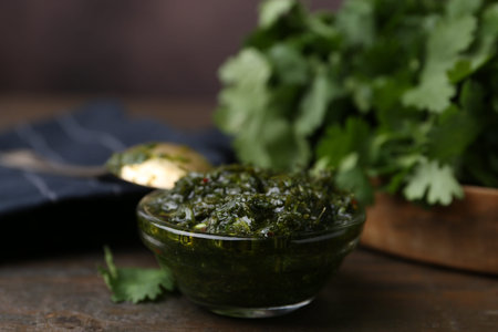 Tasty cilantro sauce in bowl on wooden table, closeup